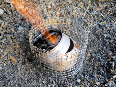 Lit soda can stove with simmer ring on top and pot stand around it